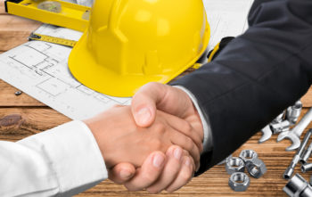 Businessman and contractor shaking hands over a hard hat