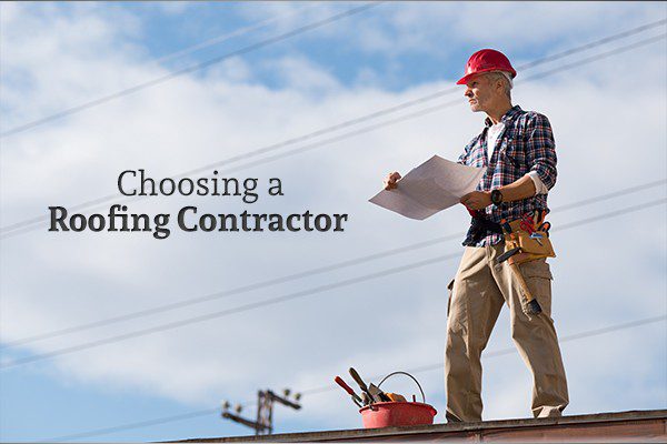 A roofing contractor with a sheet of paper and his tools stands atop a roof beside the words "Choosing a Roofing Contractor"