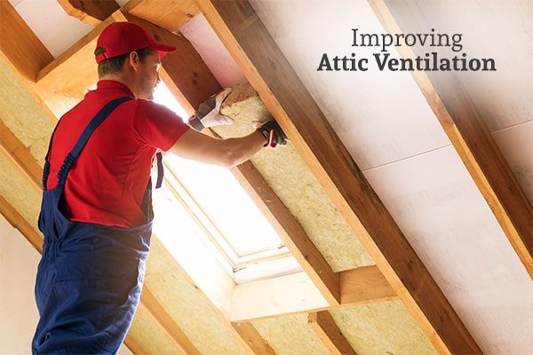 A man installing insulation in the eaves of the attic of a house beside the words improving attic ventilation