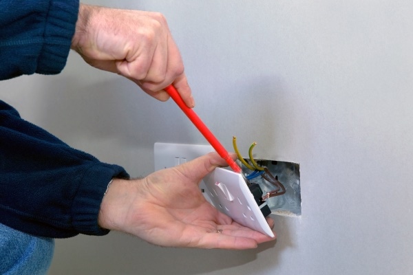 A man fixing the wiring for an outlet.
