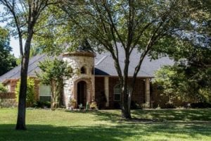 Street view of a ranch-style castle home with a new roof surrounded by nice landscaping.