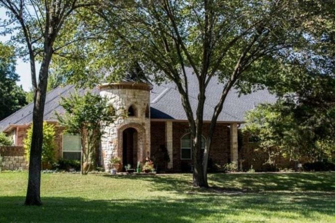 Street view of a ranch-style castle home with a new roof surrounded by nice landscaping.